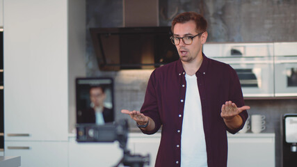 Young hipster man standing in modern kitchen recording video for internet blog