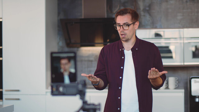 Young hipster man standing in modern kitchen recording video for internet blog