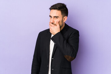 Young caucasian man isolated on purple background covering mouth with hands looking worried.