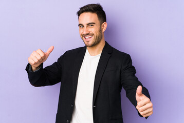 Young caucasian man isolated on purple background raising both thumbs up, smiling and confident.