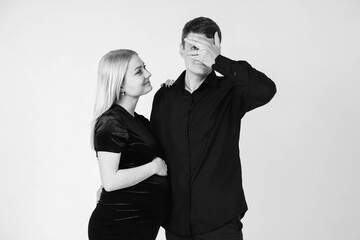 Pregnant woman and her husband smiling in black clothes on a white background. Black and white picture. Beautiful married couple. Copy, empty space for text