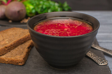 Borsch is a traditional Ukrainian soup. Vegetable soup with sour cream in a black ceramic cup on a black metal serving.