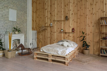 Wooden bedroom with a white fireplace. Wall with wooden panels and bricks. Near the fireplace a wooden horse. High quality photo.