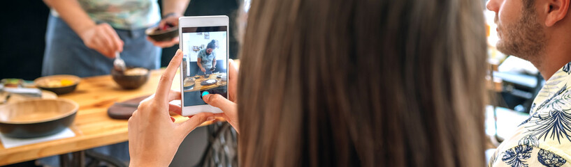 Young cook giving a cooking workshop to a group of people. Selective focus on mobile in foreground