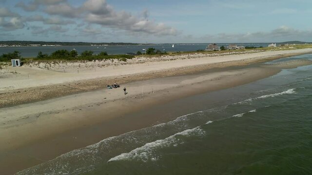 Aerial view from the ocean of a man running towards fishing rod on a lonely beach and start reeling in slow-motion on a semi-cloudy day