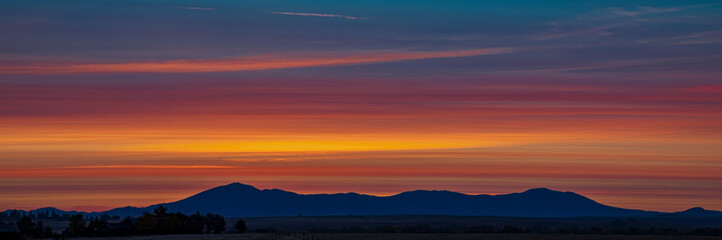 Orange Blue Hour Sunrise with layered straight line clouds and a silhouette of the Highwood Mountains in Montanan in the distance