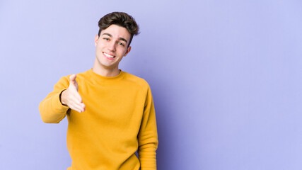 Young caucasian man isolated on purple background stretching hand at camera in greeting gesture.