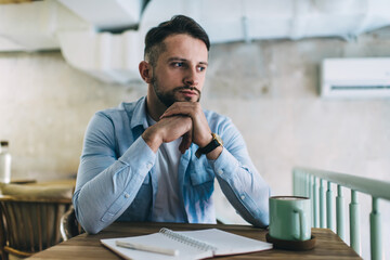 Pensive male journalist thinking over article while sitting in cafe interior