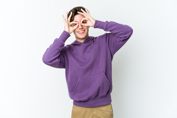 Young caucasian man isolated on white background showing okay sign over eyes