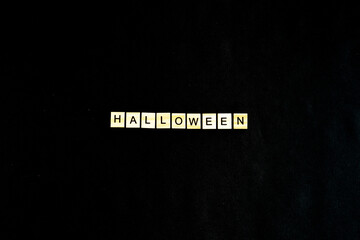 Words Halloween. Wooden blocks with lettering on black background decorated with pumpkins. Top view, flat lay. Happy Halloween