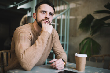 Thoughtful man with cup of coffee thinking in cafe