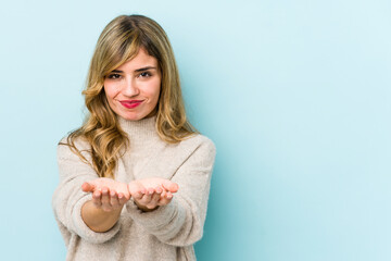 Young blonde caucasian woman holding something with palms, offering to camera.