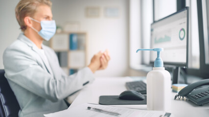 Handsome Stylish Young Man Wearing Protective Face Mask Uses Hand Sanitizer while Working at His...