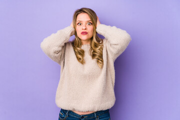 Young caucasian woman isolated on purple background covering ears with hands trying not to hear too loud sound.