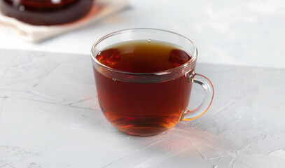 Dark tea in a glass transparent cup with hot water on a concrete background