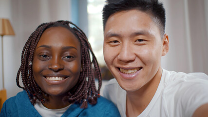 Multiethnic smiling couple taking selfie on smartphone while spending time together at home