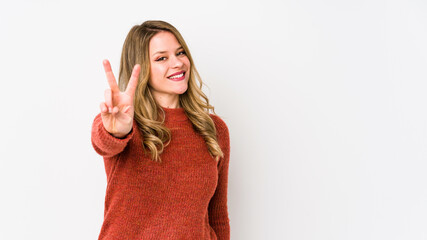 Young caucasian woman isolated on white background showing victory sign and smiling broadly.