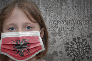 Little girl in medical mask with flag of albania stands near the old vintage wall with text coronavirus, covid, and virus picture. Stop virus concept