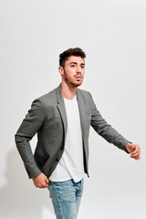 Fototapeta premium Young man wearing jeans, a white tshit iand a grey blazer walking in front of a white wall.