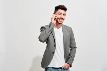 Happy young man wearing jeans, a white tshirt and a grey blazer talking with someone on his mobile...