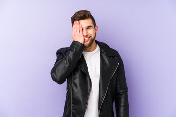 Young caucasian man isolated on purple background having fun covering half of face with palm.