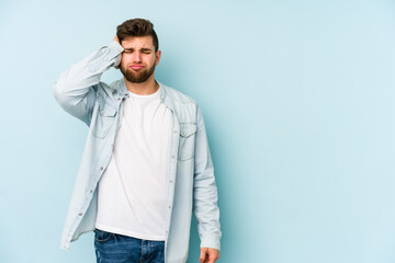 Young caucasian man isolated on blue background tired and very sleepy keeping hand on head.