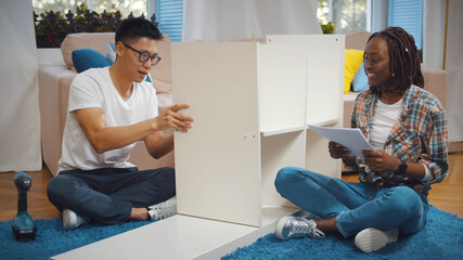 Young multiethnic family assembling furniture at new house