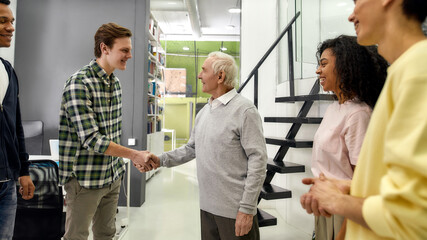 Young team greeting new worker in the modern office, Aged man, senior intern shaking hands with his colleagues