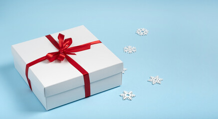 Luxury white gift box with red ribbon and White snowflakes on blue background with copy space isilated. Minimalist composition. Winter holidays concept Christmas, New Year, birthday, discounts