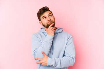 Young caucasian man isolated on pink background looking sideways with doubtful and skeptical expression.