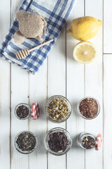 Various herbal infusions on white old wooden board with lemon and jar of honey, chamomile, red tea, rooibos, black tea, green tea, chai tea