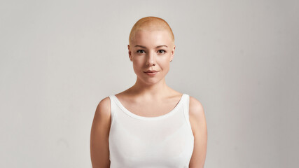 Portrait of a beautiful young caucasian woman with shaved head wearing white shirt, looking at...