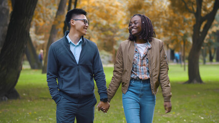 Portrait of happy multiethnic couple holding hands walking together in park