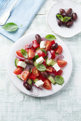 Simple salad with cherry tomatoes, feta cheese, kalamata olives, red pepper and fresh herbs. Bright wooden background. Top view.	