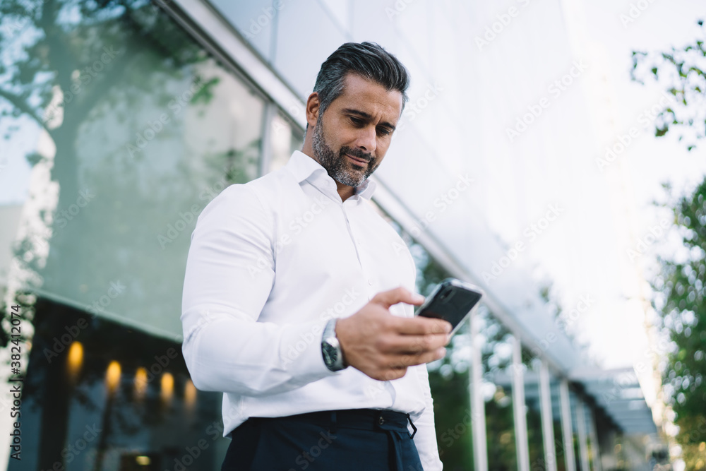 Poster below view of mature lawyer with stubble using mobile application for chatting in business chat, cau