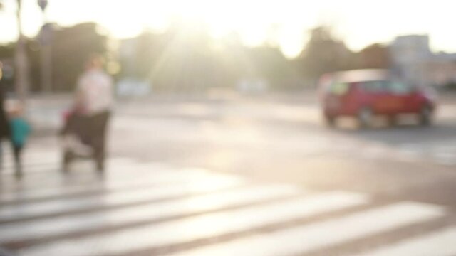 Many defocused people crossing road on zebra in sunny sunset city street