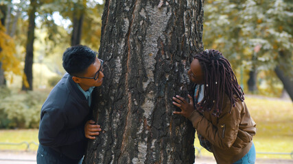 Fototapeta na wymiar Young multiethnic couple in love hugging tree trunk in autumn park