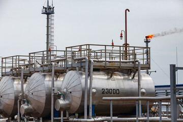 Oil refinery plant. Heat exchangers, lighting mast, platforms and orange gas torch on grey sky background.