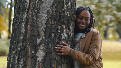 Casual cheerful african woman embracing tree in park