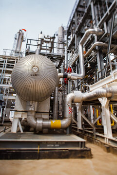 Uralsk region, Kazakhstan - May 24 2012: Oil refinery plant in desert. Worker or engineer in red work wear and white helmet. Heat exchanger and pipelines. Tilt-shift photo. Partially blurred.