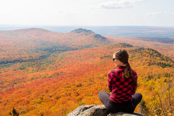 Naklejka na ściany i meble Back view of a young woman sitting in the Mégantic national park and admiring the autumnal colors, Canada