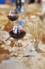 Close up of a glass of delicious red wine on concrete table with bread sticks during wine tasting tour. Sampling  in winery. Copy space for the text. Menu design. Creative bar menu background.