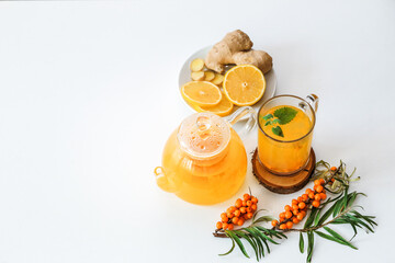 Hot sea buckthorn tea with lemon, ginger and honey on a white table top view. Twigs and berries of sea buckthorn