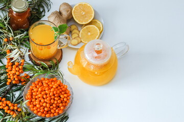 Hot sea buckthorn tea with lemon, ginger and honey on a white table top view. Twigs and berries of sea buckthorn