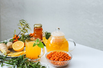 Hot sea buckthorn tea with lemon, ginger and honey on a white table