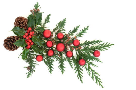 Christmas decorative arrangement with winter holly, pine cones, cedar cypress & red bauble decorations on white background. Festive themed element. Flat lay, top view, copy space.