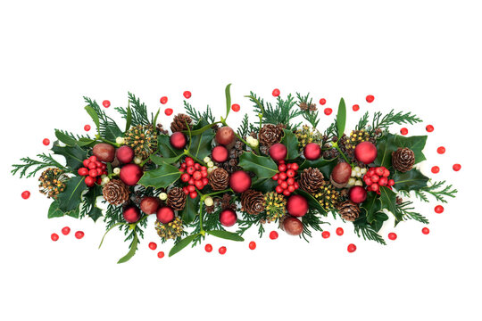 Christmas decorative display for the festive season with red bauble decorations holly & loose berries, mistletoe, acorns & cedar cypress on white background. Xmas and New Year theme. Top view.