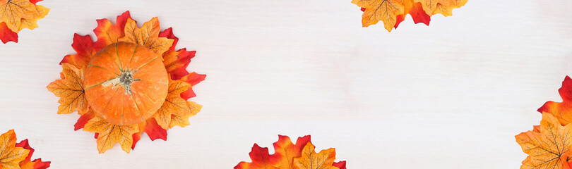 Autumn leaves and pumpkin over wooden background with copy space.