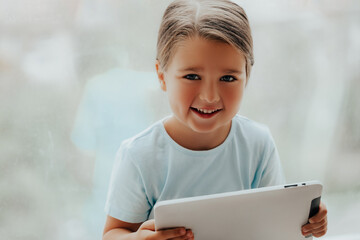 Cute Little Girl with Tablet pc Relaxing in a spacious room near the Window 