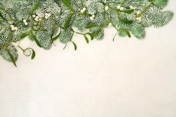 Fir & mistletoe border on old parchment paper background. Traditional winter solstice & Christmas greenery for the festive season and New Year, Top view, flat lay, copy space.

